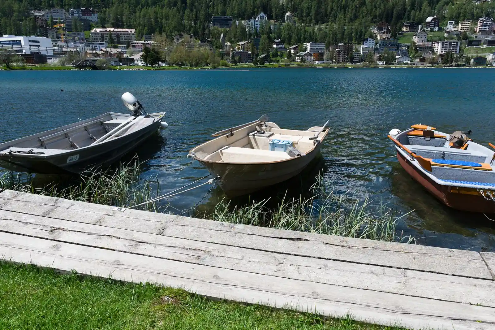 Trois barques à moteur amarrées le long d'un ponton sur un lac, village en arrière-plan