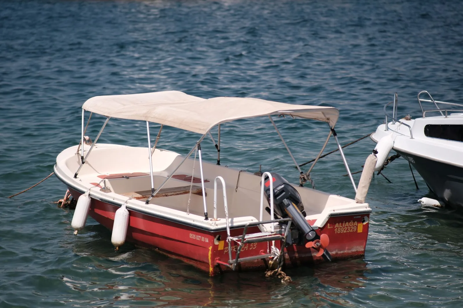 Petit bateau à moteur avec capote amarré sur l'eau, pare-battages visibles