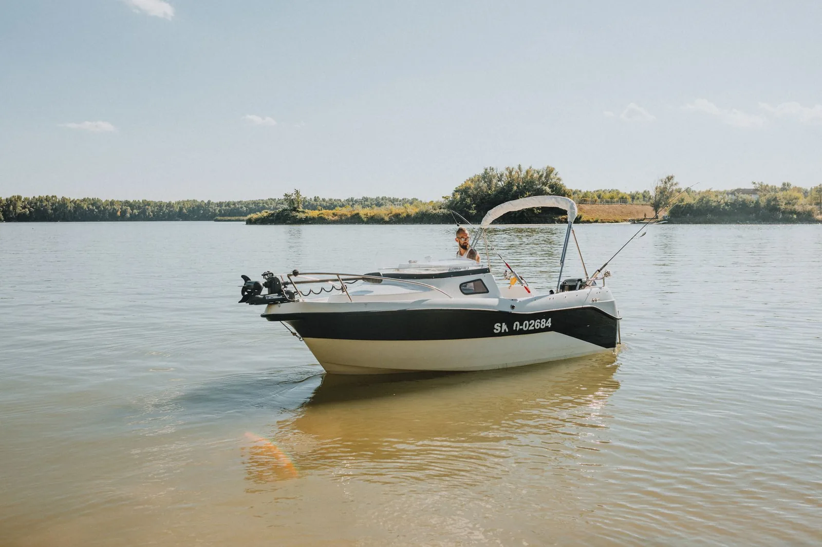 Bateau à moteur à l'ancre dans le calme d'un lac, rive boisée au fond