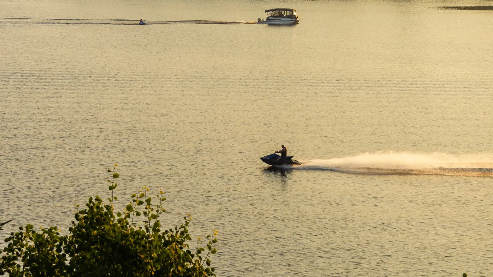 Jet-ski filant sur un lac au coucher du soleil, entre forêts et un bateau au loin