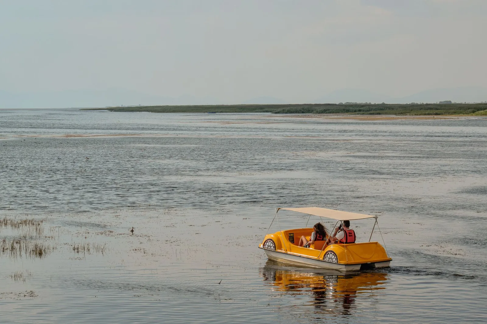 Pédalo jaune avec capote naviguant sur un grand lac calme