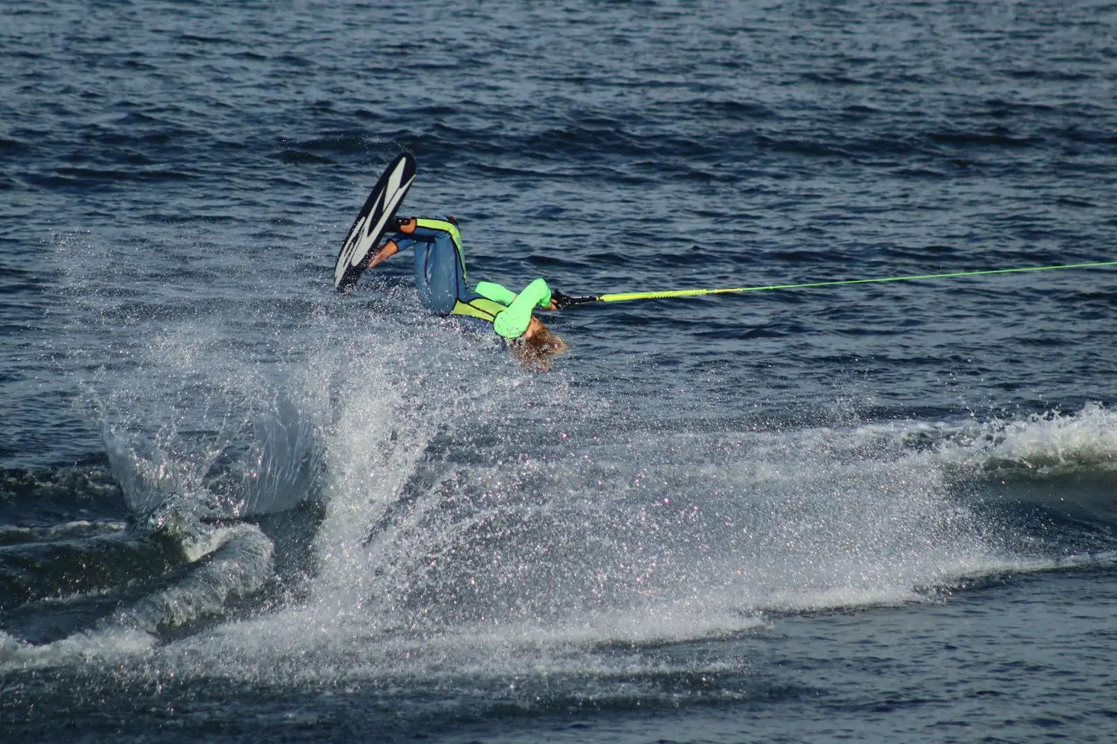 Skieur nautique en pleine figure, ski au pied et corde tendue, dans une gerbe d'eau