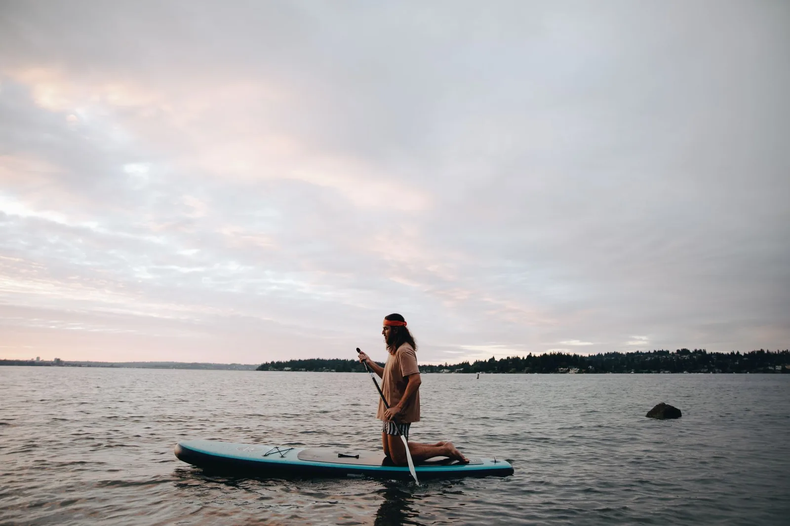 Pagayeur à genoux sur sa planche de paddle, pagaie en main, sur un lac calme en soirée