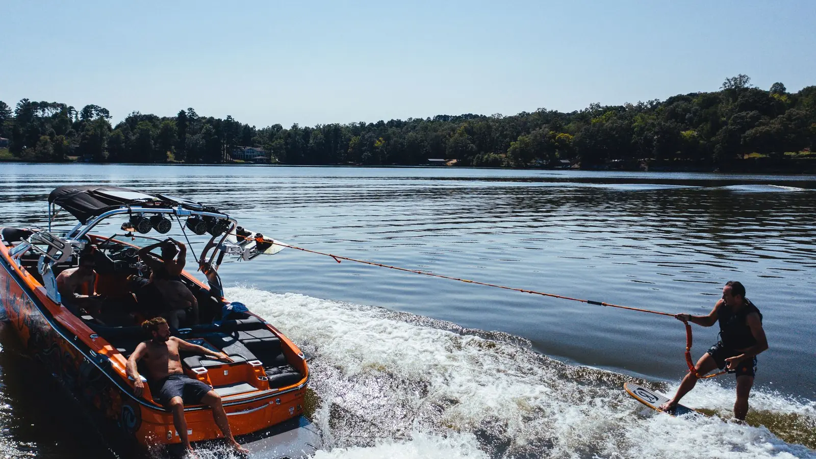Wakeboardeur tiré par la corde d'un bateau sur un lac bordé de forêt