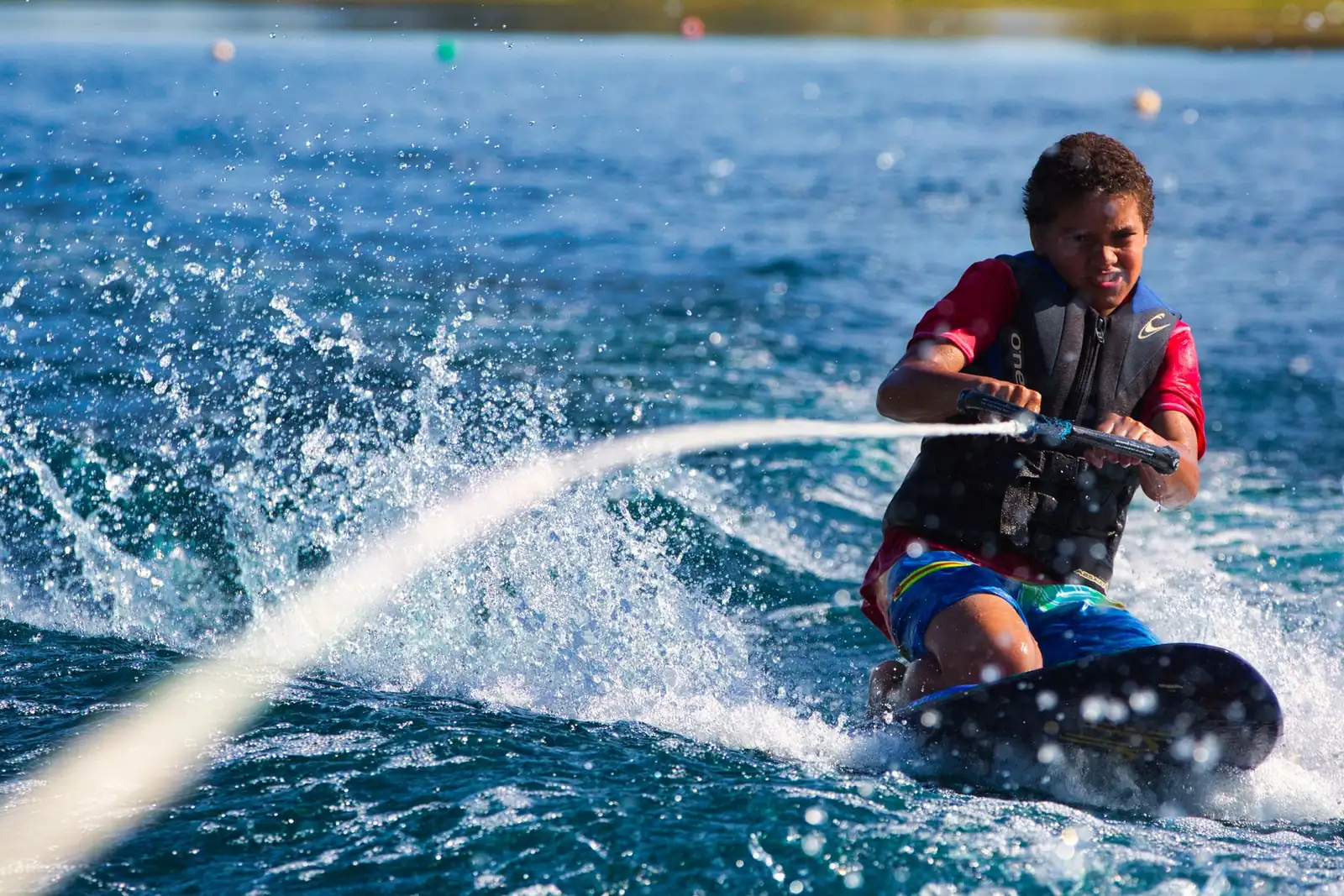Jeune wakeboardeur en gilet de flottaison dans les éclaboussures, tenant la poignée de traction