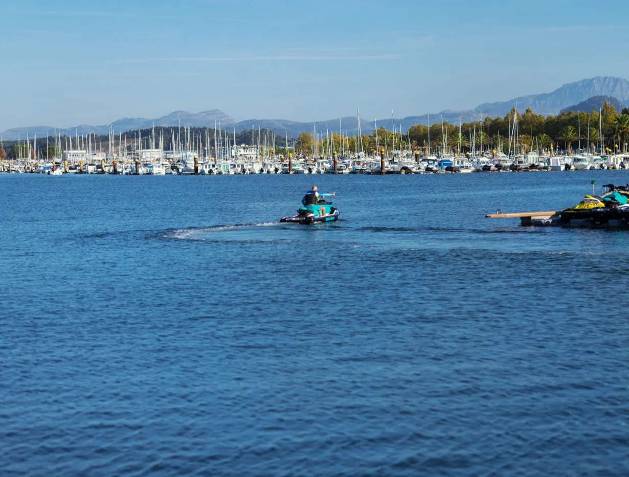 Jet-ski quittant un ponton de location dans un port de plaisance, montagnes en arrière-plan