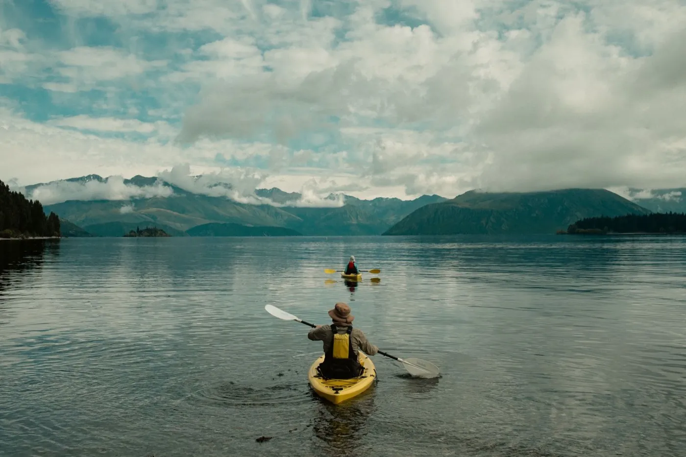 Deux kayakistes pagayant sur un lac calme entouré de montagnes