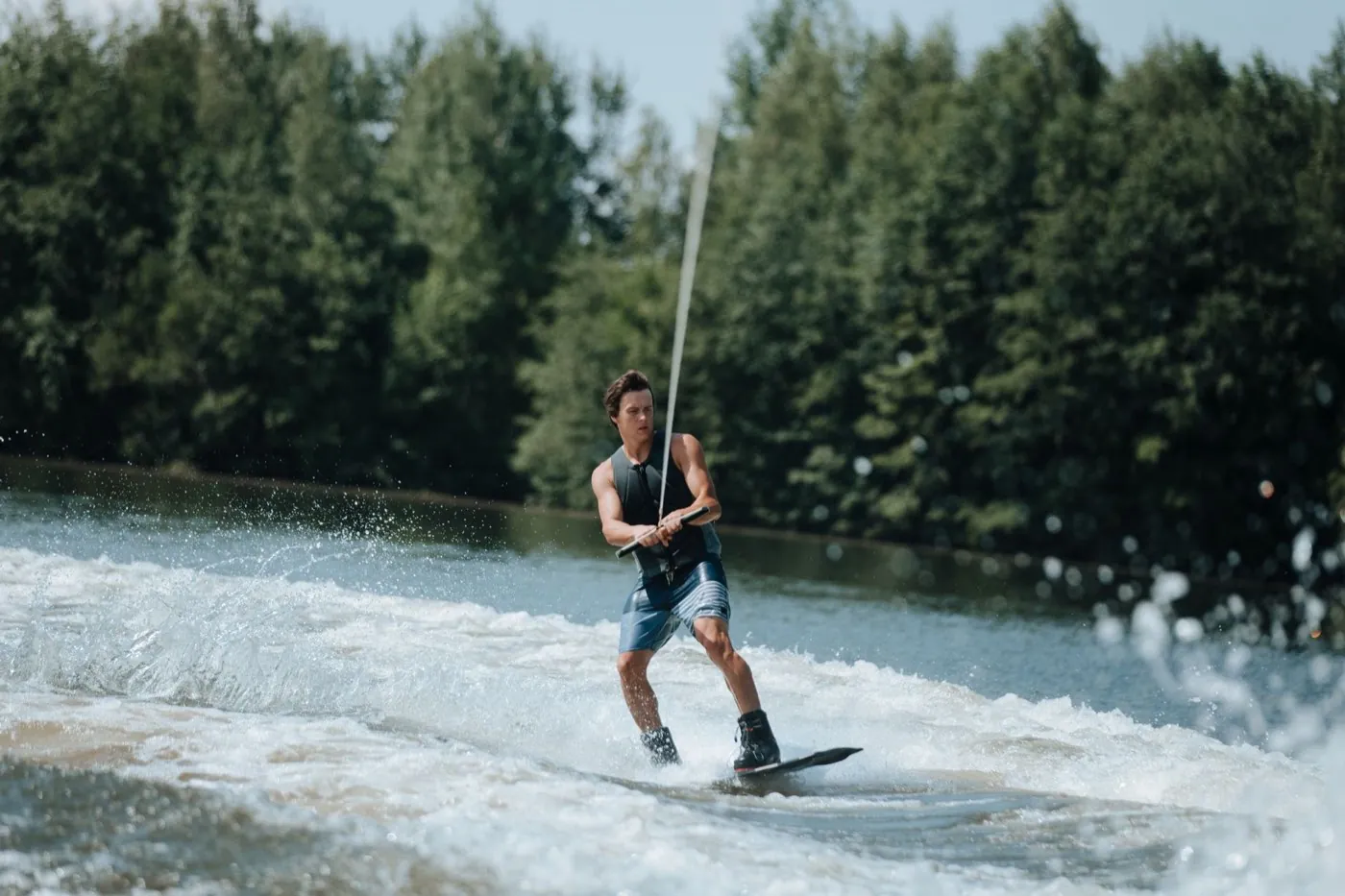 Wakeboardeur en pleine session derrière un bateau, gerbes d'eau autour de la planche